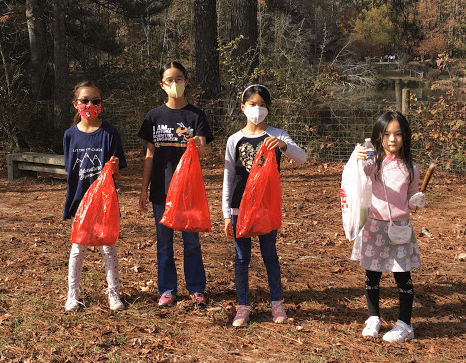Four young volunteers holding filled red litter bags in a park