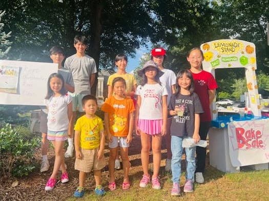 Children and volunteers standing behind a neighborhood lemonade stand