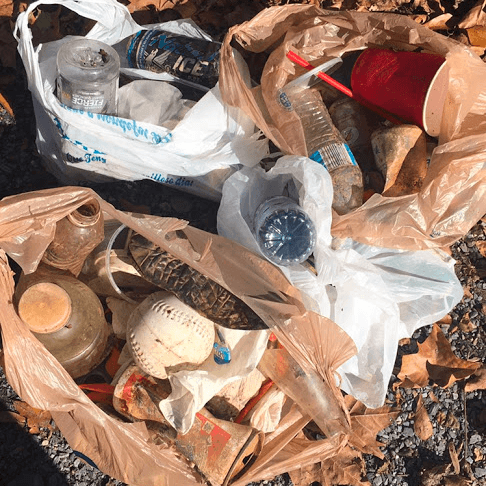 A filled cleanup bag beside litter collected from a wooded area